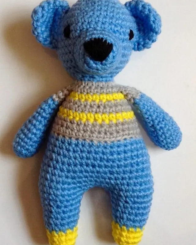 A blue crocheted bear in a striped top with a black nose