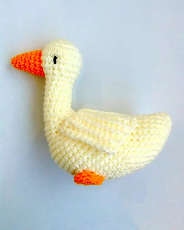 A cream crocheted goose with an orange beak