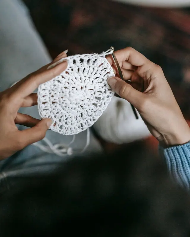 Hands holding a small white crochet circle and hook