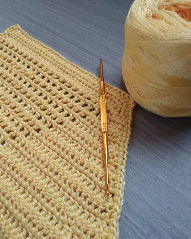 A yellow crochet swatch with a hook and a yarn ball