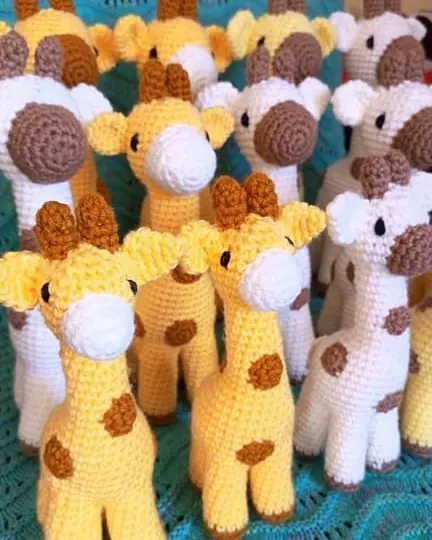 Crocheted giraffes in yellow and cream with brown spots and white muzzles, standing together on a teal blanket