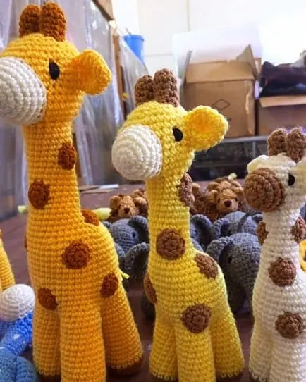 Three crocheted giraffes in different sizes and shades of yellow and cream standing together
