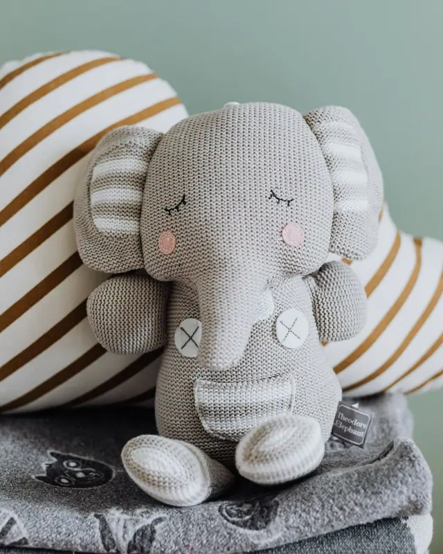 A grey elephant toy leaning on a striped cloud cushion