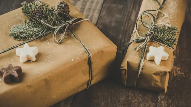 Two gifts in kraft paper with pine sprigs and twine on dark wood