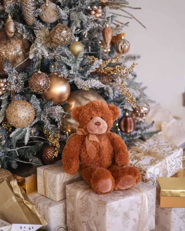 A brown teddy bear beside gifts under a decorated tree