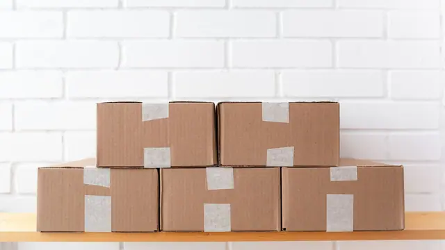 Stacked taped cardboard boxes on a wooden shelf against white brick