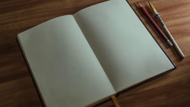An open sketchbook with pencils on a wooden desk