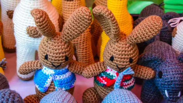 Two brown crocheted rabbits with long ears, one in a blue waistcoat and one in a red and green one, among other animals