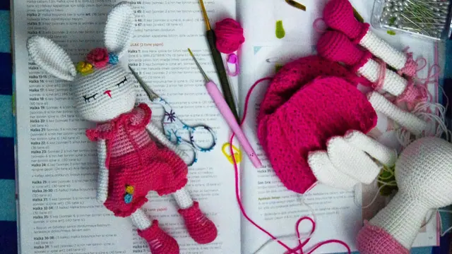 A crochet bunny doll with hooks on an open pattern book