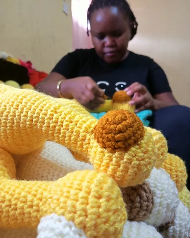 Young woman in a black t-shirt stitching crocheted yellow giraffe pieces, ready to assemble