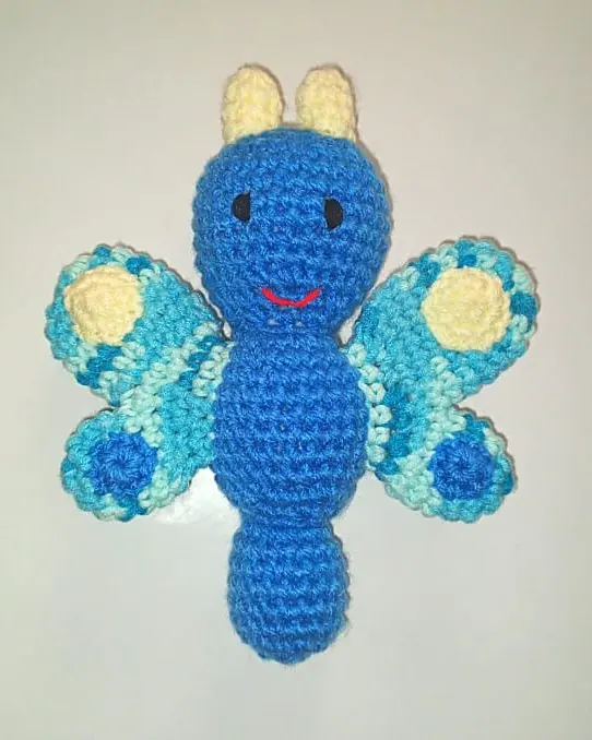 A blue crocheted butterfly with yellow spots on its wings