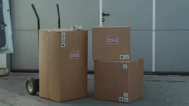 Three cardboard parcels on a hand trolley beside a van