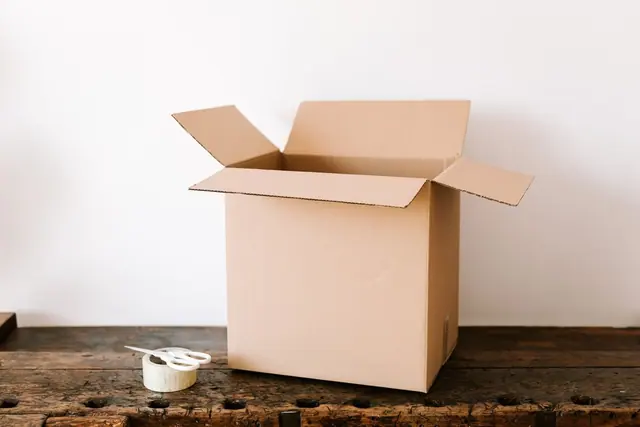 An open cardboard box on a wooden desk with tape and scissors
