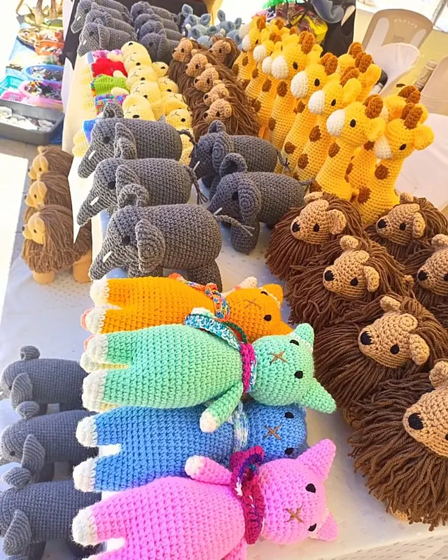 Table of crocheted lions, giraffes and grey elephants with four long cats in orange, mint, blue and pink lying at the front
