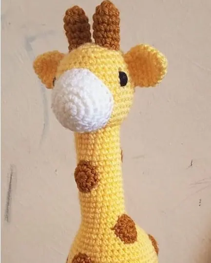 A crocheted yellow giraffe with brown spots and a white muzzle