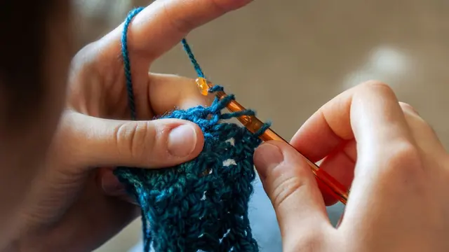 Hands crocheting teal blue yarn with an orange hook