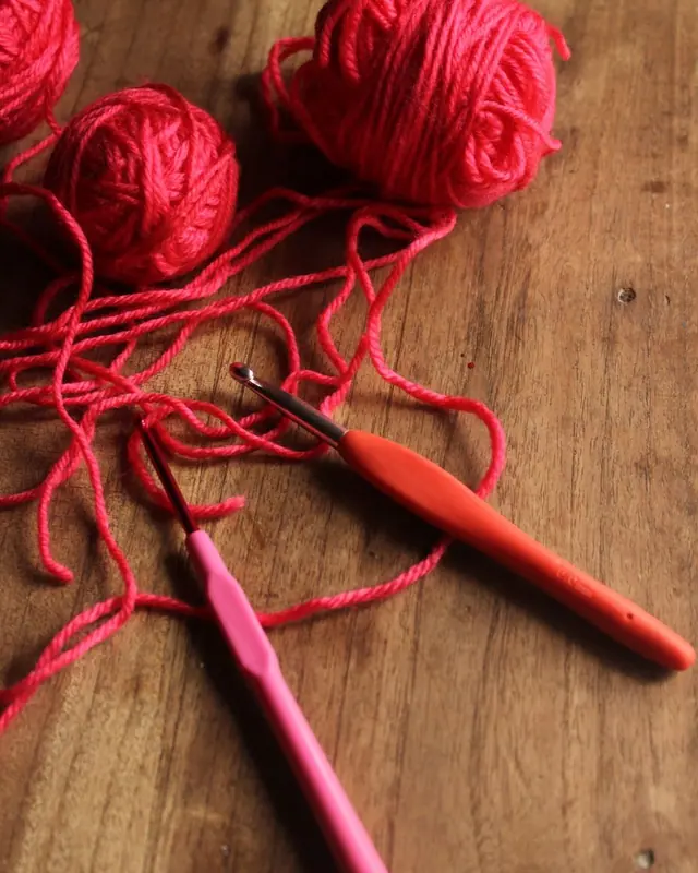 Red yarn balls and crochet hooks on a rustic wooden table