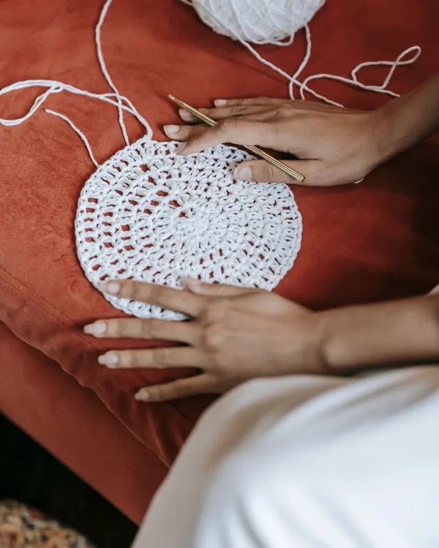 Hands working a white crochet piece on a terracotta red cloth