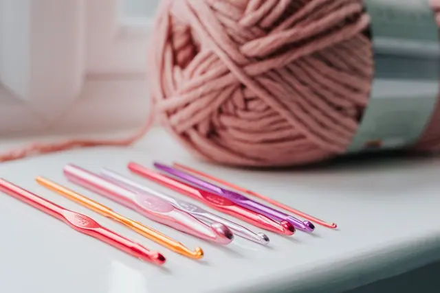 Coloured crochet hooks beside a pink yarn ball on a windowsill
