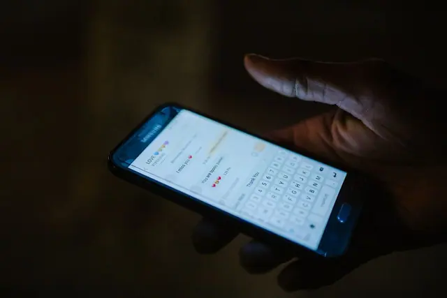 A hand holding a phone with a messaging screen in dim light