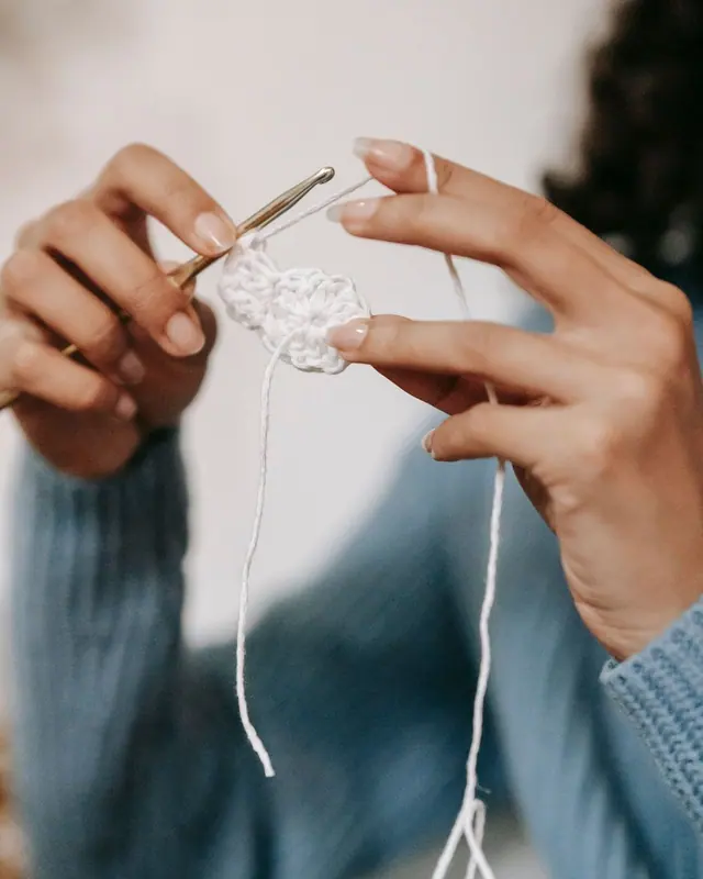 Hands in a blue sleeve working white yarn with a hook