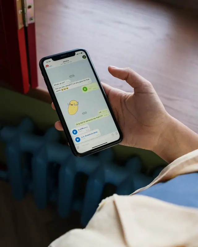 A hand holding a phone with a chat list, face not shown