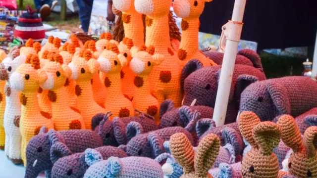 Market stall packed with orange giraffes, grey and purple elephants and brown rabbits with shoppers behind