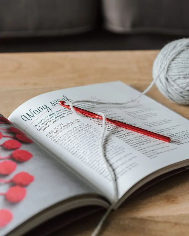 A grey yarn ball and red pencil on an open book