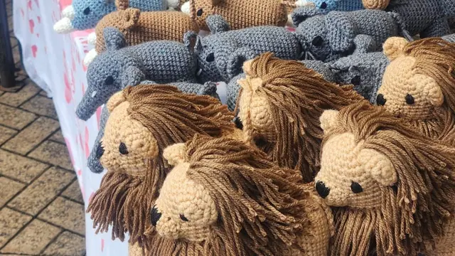 Table with crocheted lions at the front and rows of yellow and cream giraffes at the back