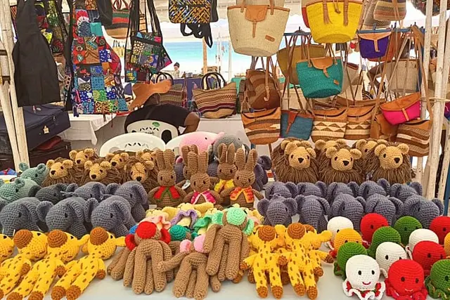 Stall under a white canopy with bags hanging above and rows of crocheted animals below