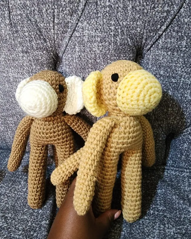 Hand holding two crocheted long armed monkeys