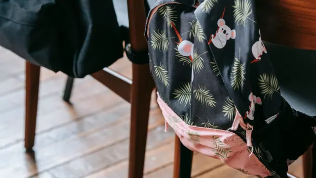A wooden school desk with bags hanging off the chairs