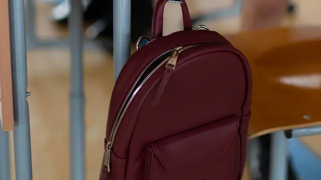 A burgundy backpack hanging on a school desk