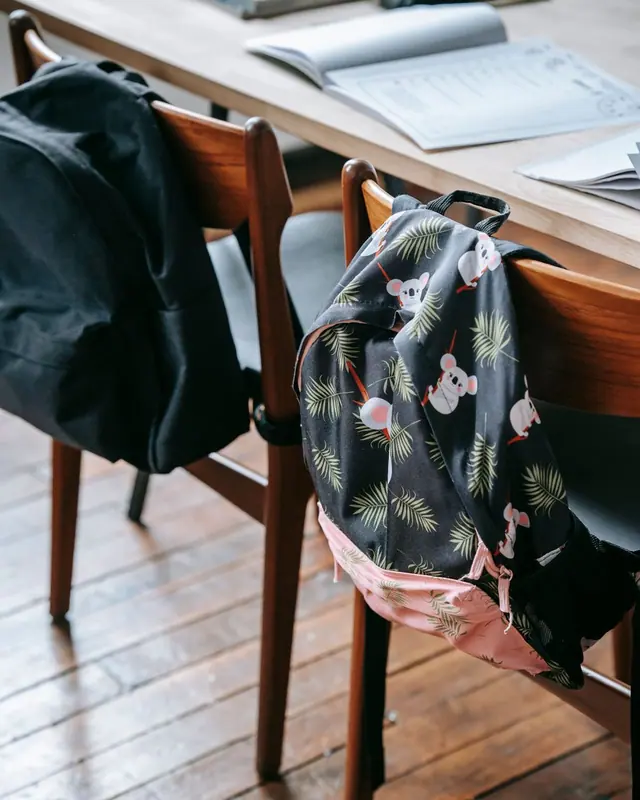 A wooden school desk with bags hanging off the chairs