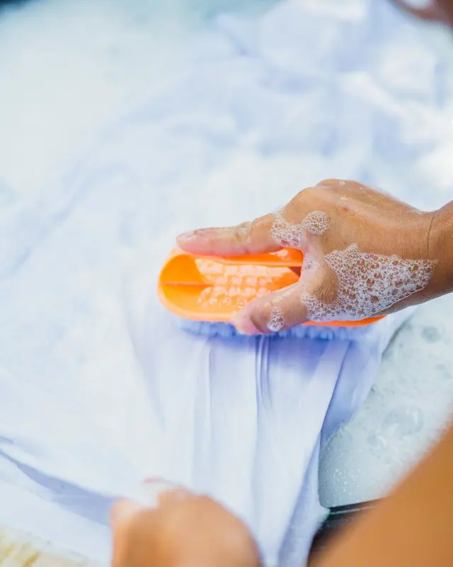 Hands scrubbing light blue cloth with soap bubbles