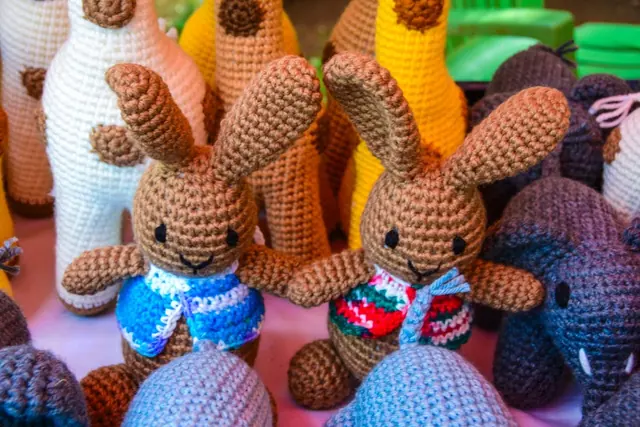Two brown crocheted rabbits with long ears, one in a blue waistcoat and one in a red and green one, among other animals