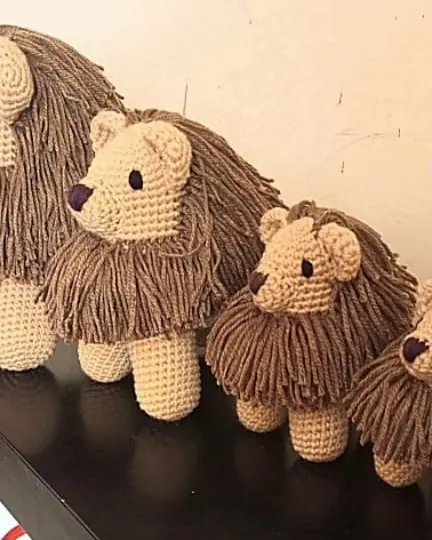 Row of crocheted tan lions with brown manes on a dark table, getting smaller from left to right