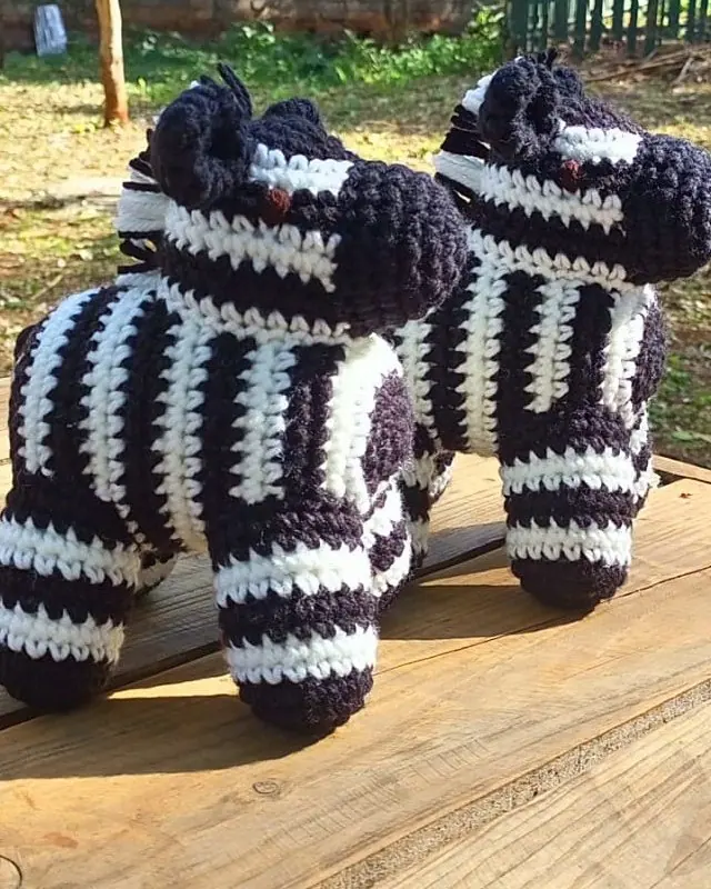 Two crocheted black and white zebras standing on a wooden table