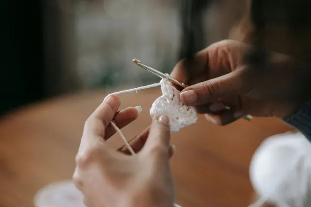 Close view of hands holding a crochet hook and white cotton