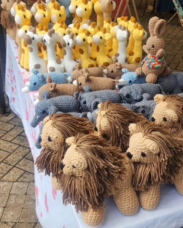 Table with crocheted lions at the front and rows of yellow and cream giraffes at the back