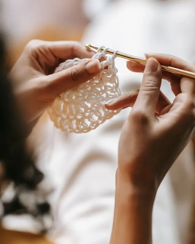 Hands crocheting a small white piece in soft light