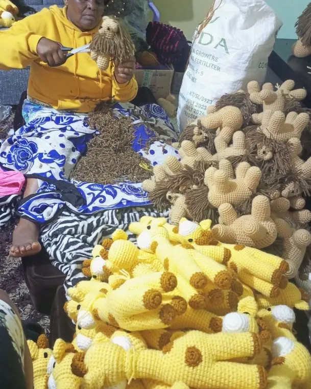 Woman in a yellow hoodie trimming a lion mane with scissors among piles of crocheted giraffe and lion pieces