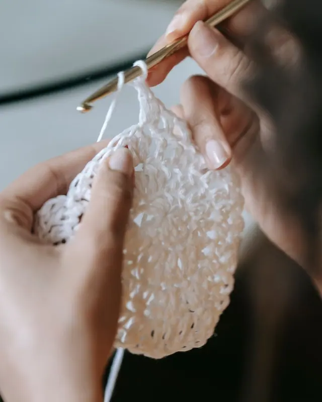 Hands crocheting white yarn in a vertical close up