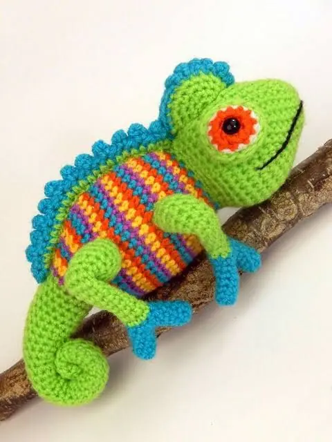 Bright green crocheted chameleon with a striped body perched on a branch