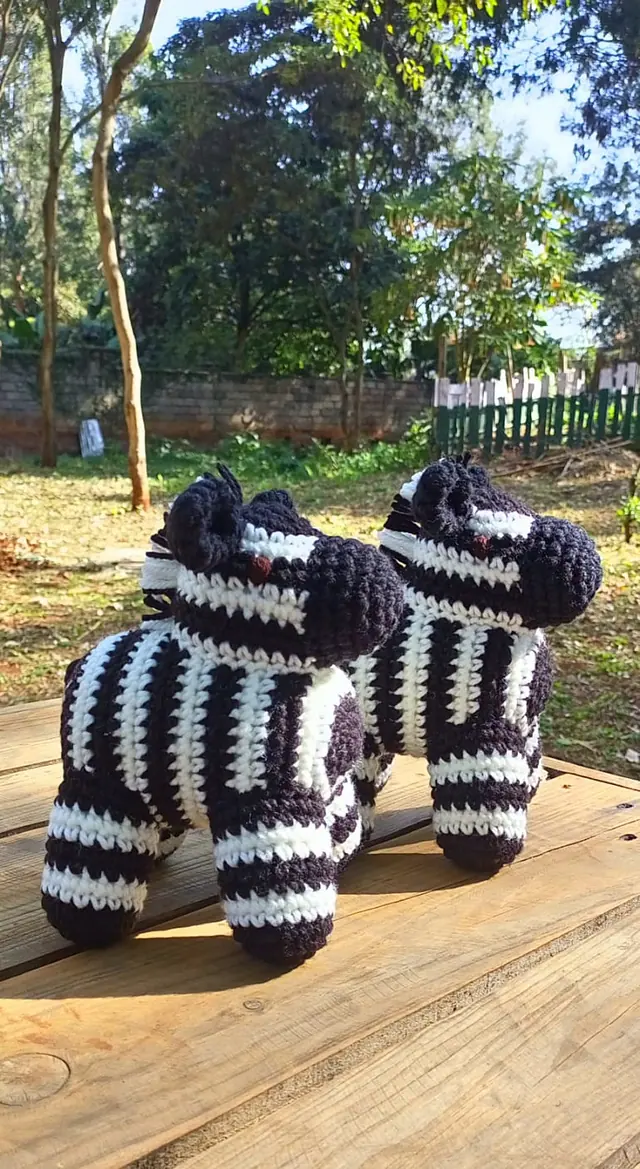 Two crocheted black and white zebras standing on a wooden table in a sunny garden