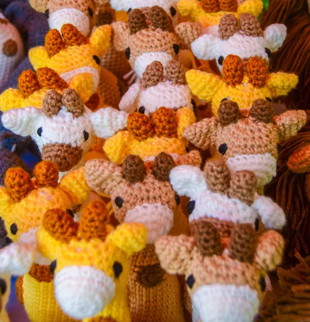 Close view of many crocheted giraffe heads in yellow, tan and cream with brown and orange horns, mostly out of focus