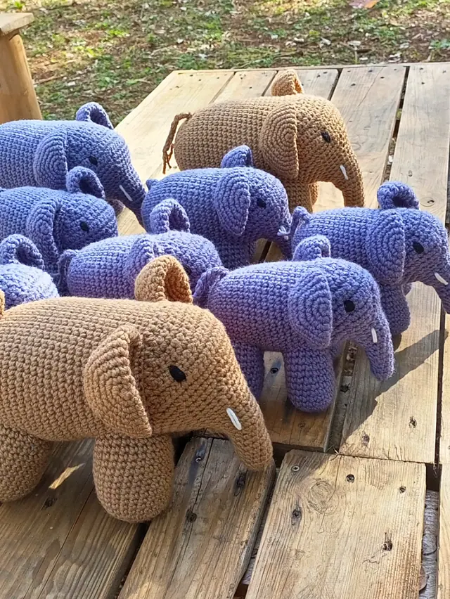 A herd of crocheted elephants in lavender purple and caramel brown on a wooden table outdoors