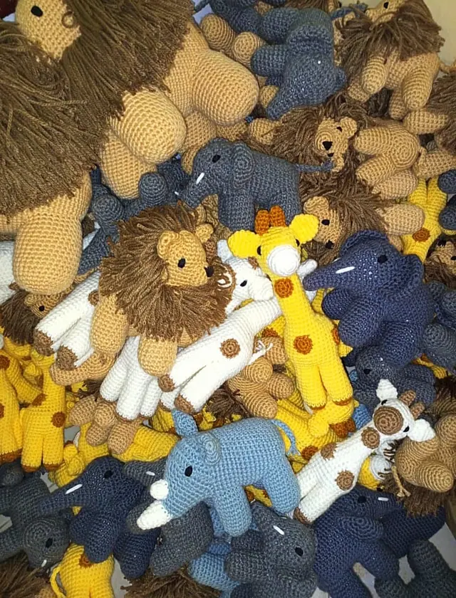 Large pile of crocheted lions, elephants and giraffes in tan, grey, navy, light blue, yellow and white