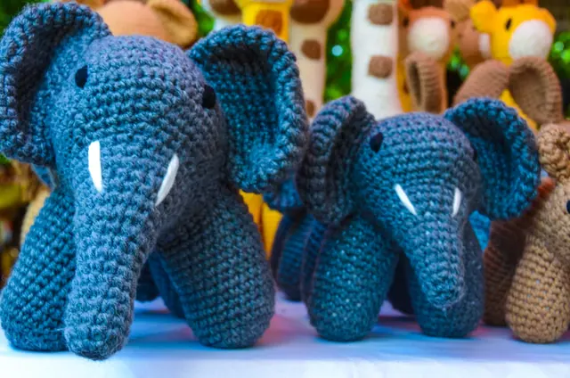 Close-up of two slate blue crocheted elephants with white tusks standing on a stall table