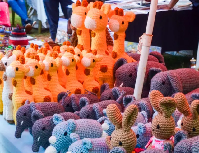 Market stall packed with orange giraffes, grey and purple elephants and brown rabbits with shoppers behind